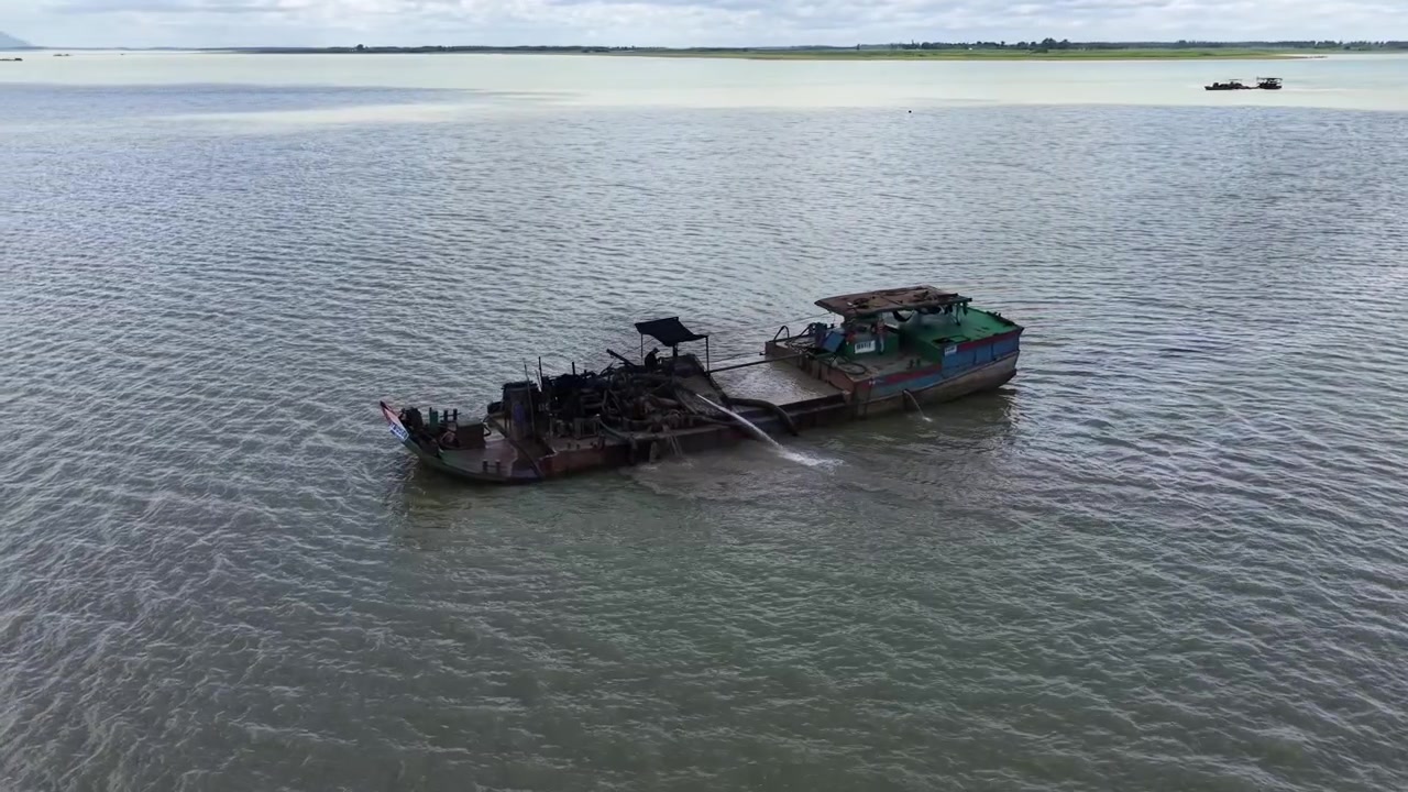 Lenta orbita di un drone attorno a una draga per sabbia e una chiatta in acque aperte, con il Monte Ba Den che appare all'orizzonte dietro, Dau Tieng, Tay Ninh, Vietnam.