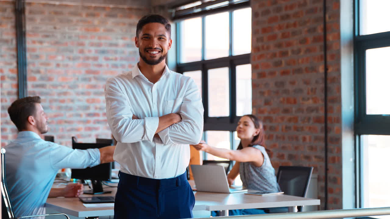 retrato de un hombre de negocios sonriente de pie en una oficina ocupada con colegas trabajando en el fondo