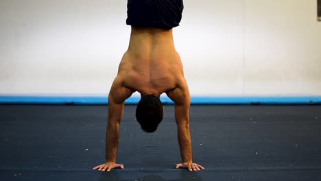 a still shot of a shirtless muscled guy doing handstands in gymnastics gym