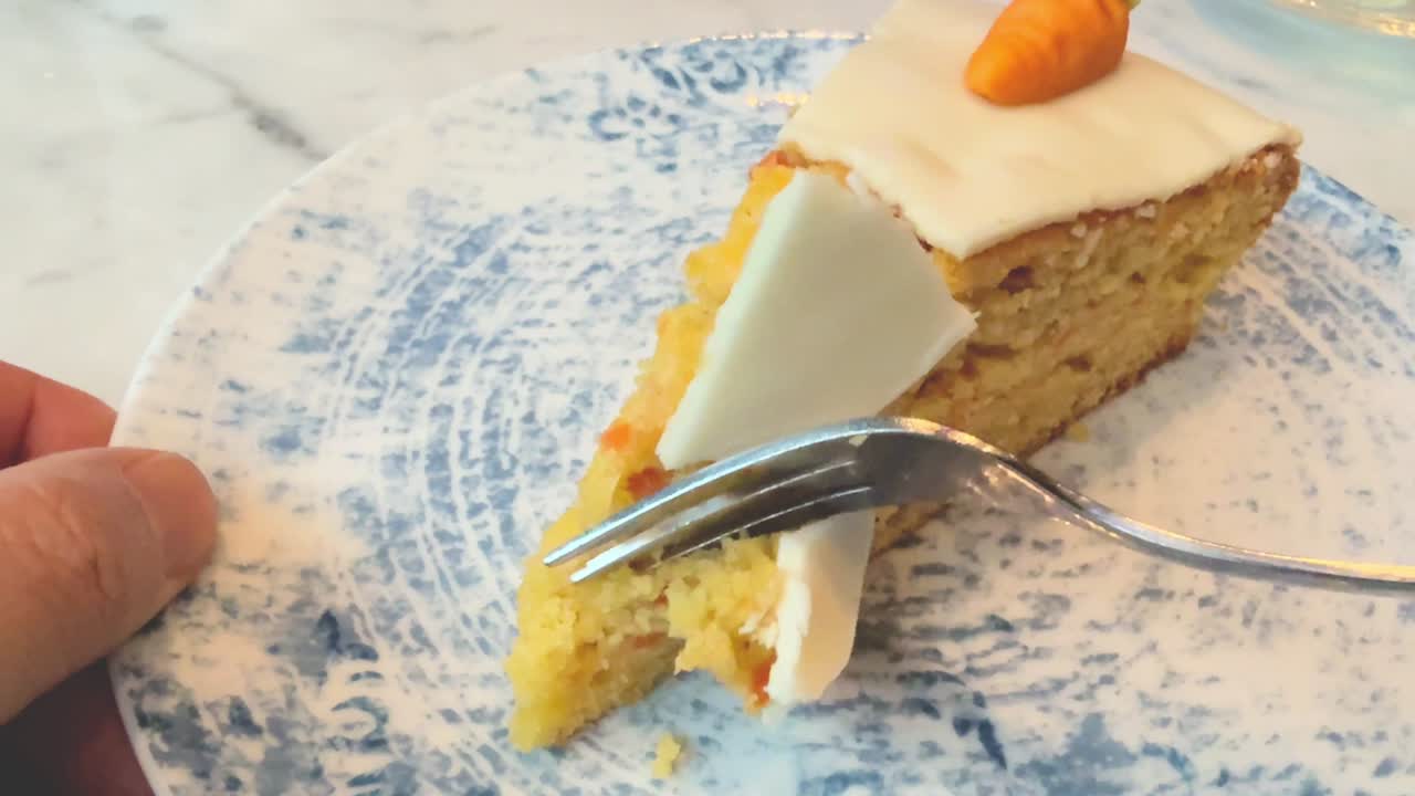 Eating a piece of carrot cake close up on a blue ceramic plate with little marzipan carrot decoration