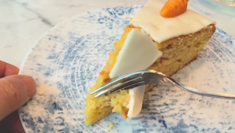eating a piece of carrot cake close up on a blue ceramic plate with little marzipan carrot decoration