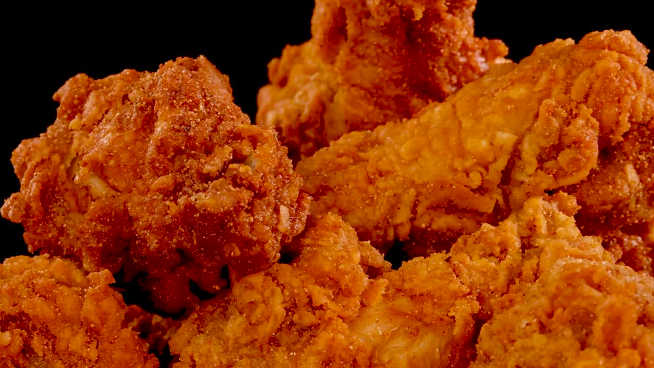 Scatto macro di pollo fritto croccante e condito che ruota lentamente su uno sfondo scuro.