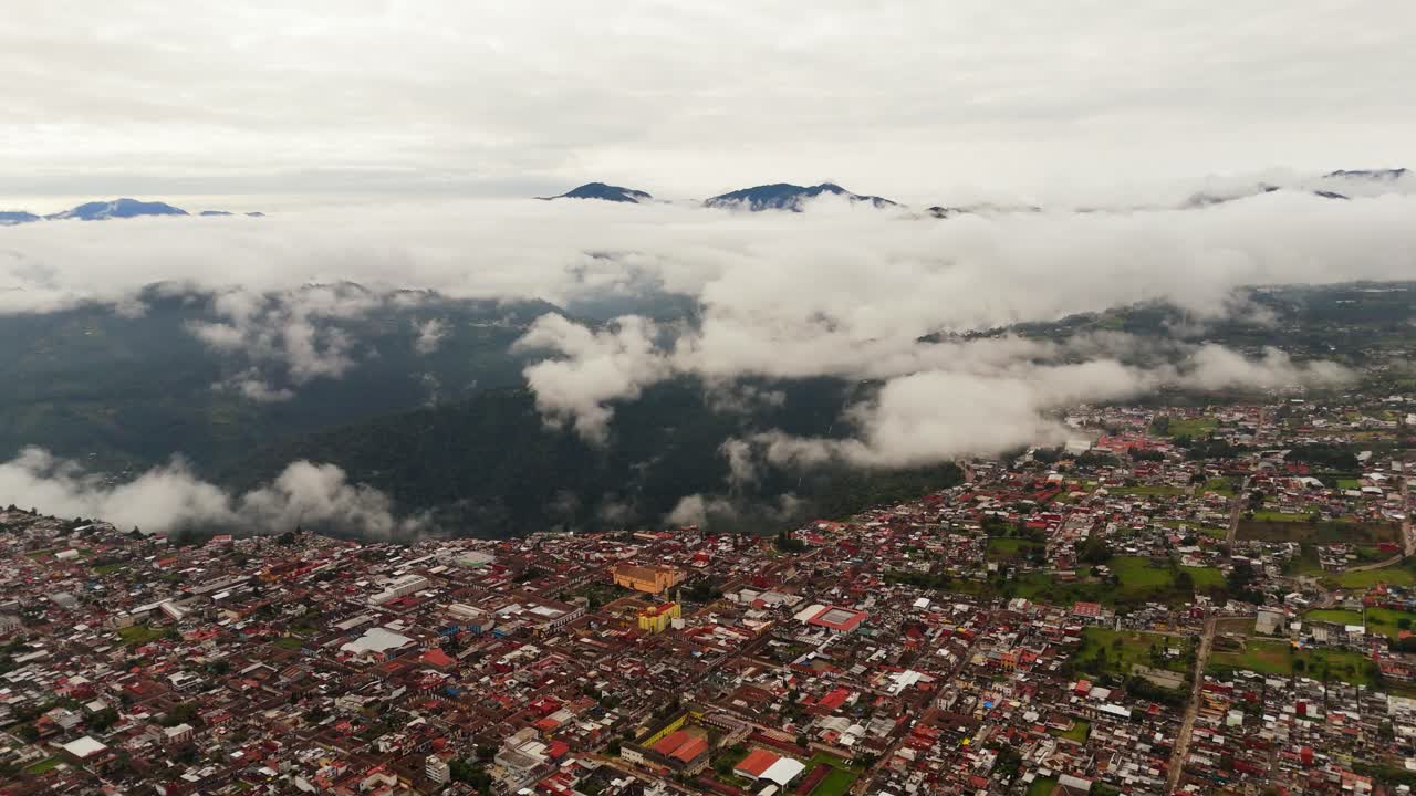 High drone shot advancing above Zacatlán, showing the city beneath drifting clouds and the surrounding mountains in a deep top-down view