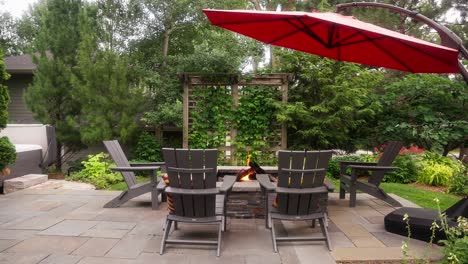 static-shot-of-a-propane-fire-pit-surrounded-by-Adirondack-chairs-with-a-large-red-umbrella-on-a-patio-during-the-day