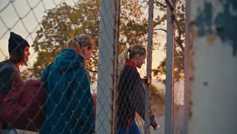 A-happy-blonde-girl-together-with-her-friends-with-a-basketball,-enters-a-special-basketball-court-fenced-with-a-grid-for-playing-basketball-early-in-the-morning-at-sunrise