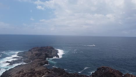 Dron-Ascendiendo-Sobre-Una-Península-Rocosa-Que-Muestra-El-Océano-Pacífico-Al-Fondo-Mientras-Las-Olas-Aplastan-Las-Rocas