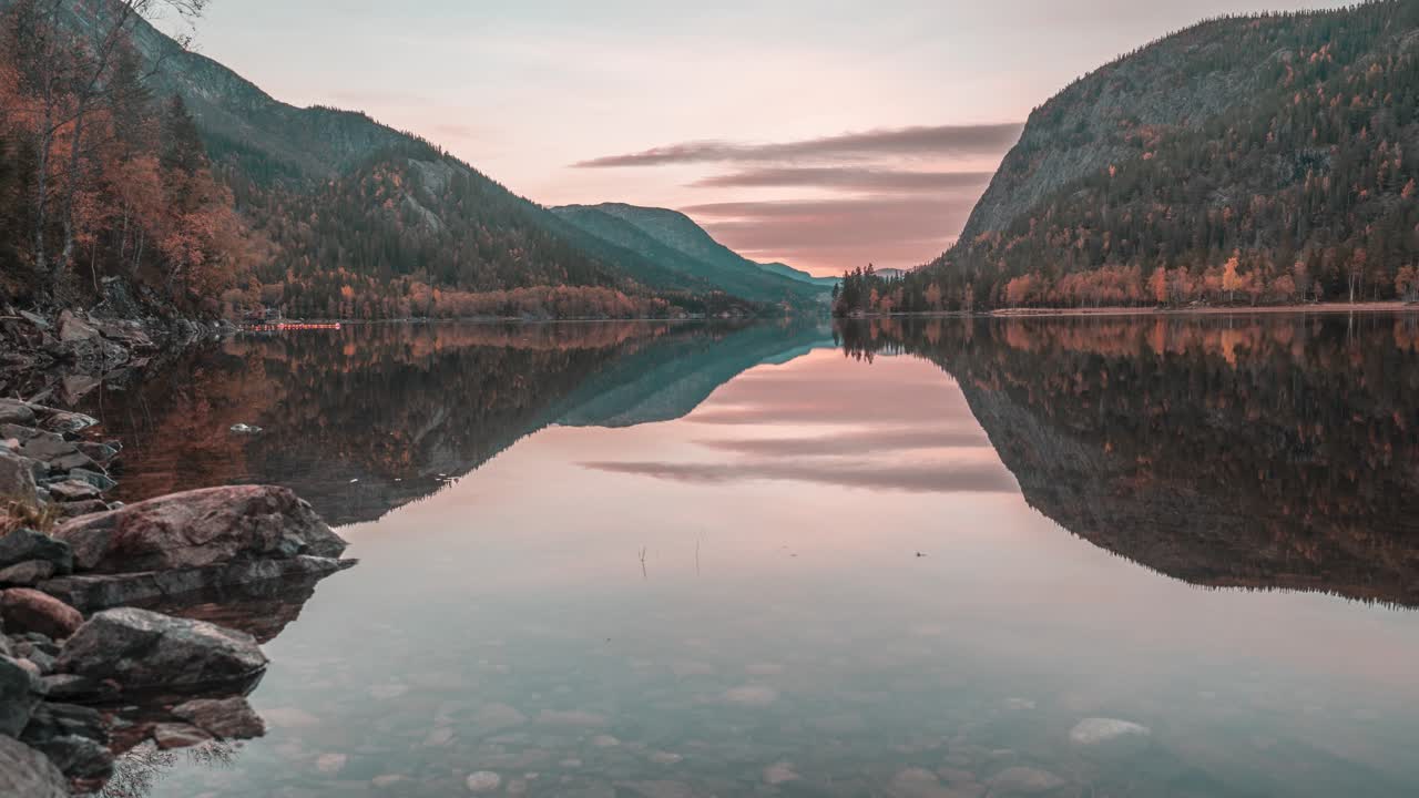 Pink skies and forest-covered mountains reflected in the still mirrorlike waters of the shallow lake