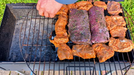 marinated cuts of meat are carefully placed by hand onto a hot grill in a backyard setting