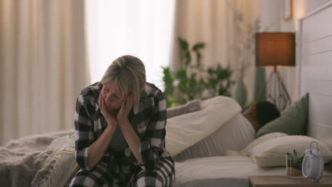 upset woman in bedroom while man sleeps