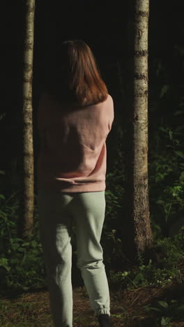 sad young woman in home clothes looks thoughtfully into dark thickets of forest. lady enjoys nature and thinks about life while standing near stairs of house