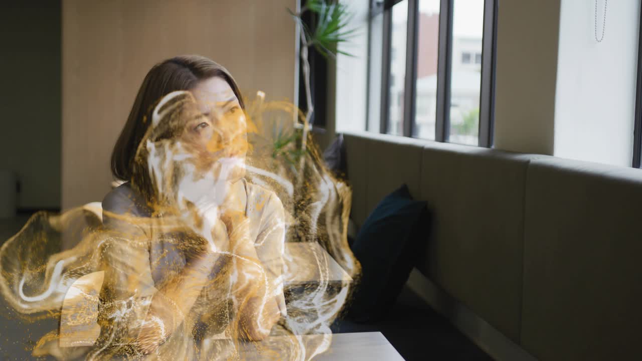 Femme assise près de la fenêtre, levant la main vers sa mâchoire, générant une aura dorée tourbillonnante pour la santé.