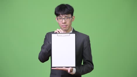 young asian businessman showing clipboard to camera