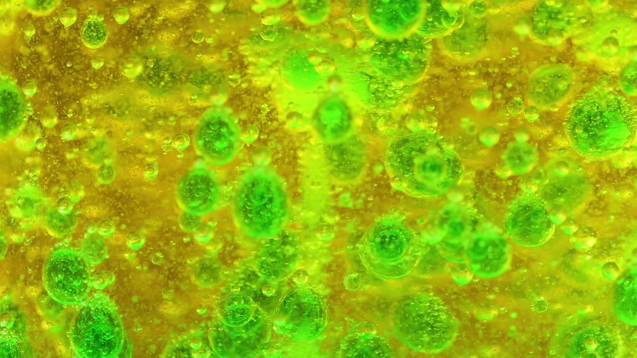 Close-up view of dynamic green bubbles in a yellow liquid, showcasing vibrant colors and fluid motion.