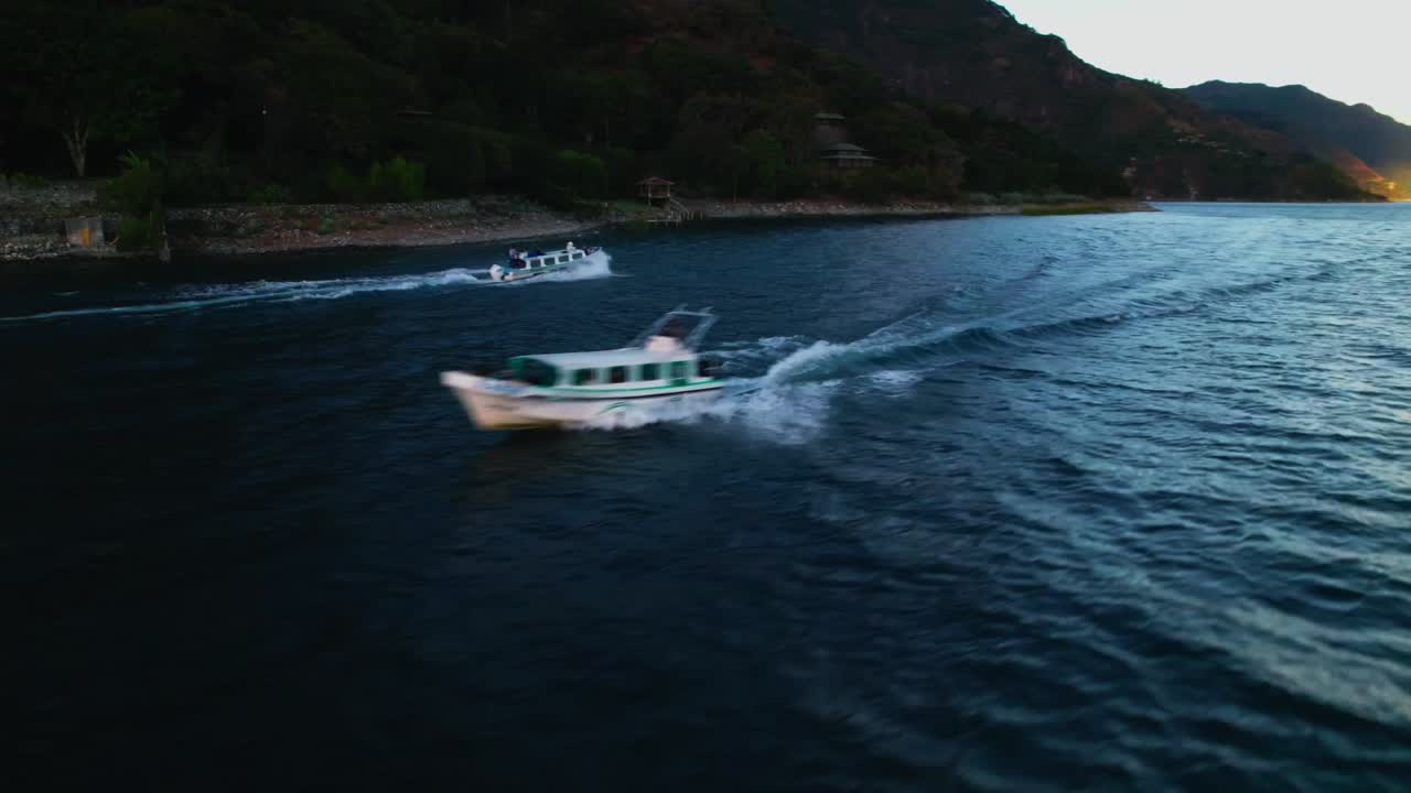 Drone in semi-orbita che segue un motoscafo vicino alla costa del lago di Atitlán, con acqua e montagne texturizzate