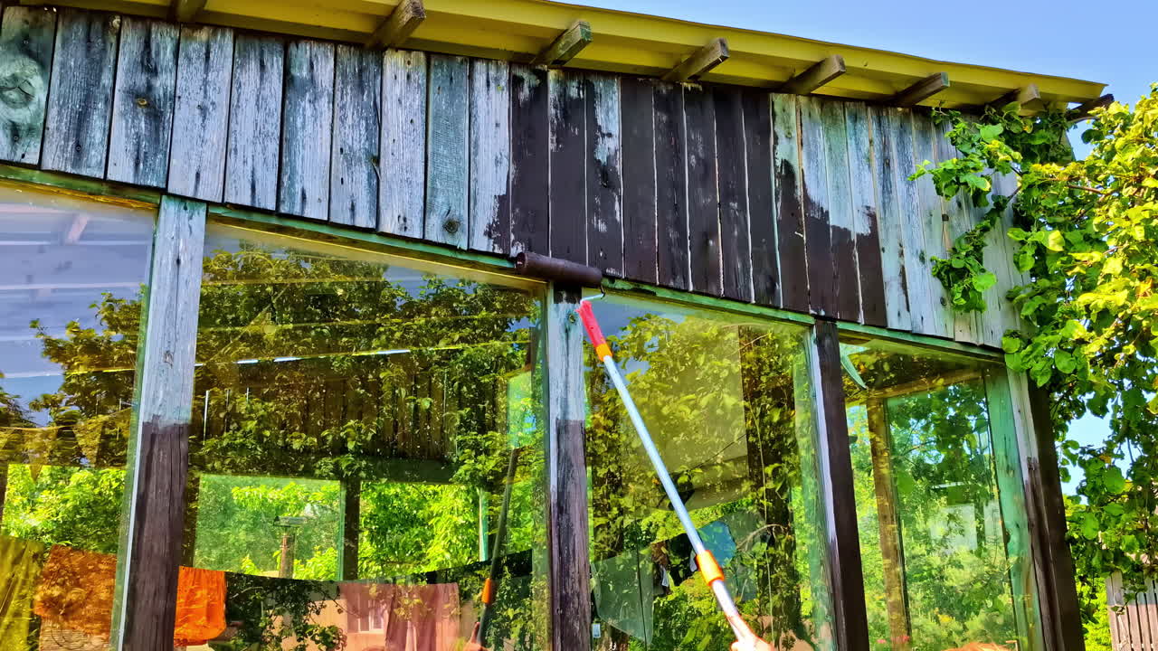 Woman staining upper wood siding of garden shed with roller pole