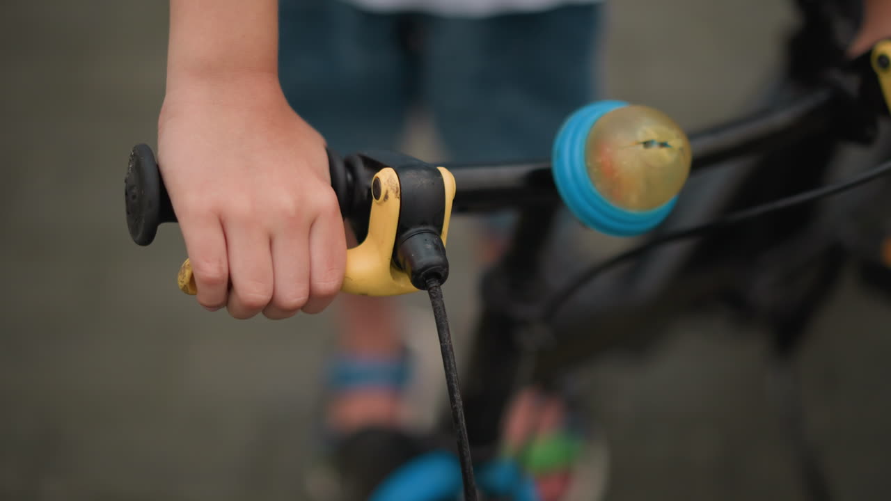 un primer plano de la mano de un niño agarrando el freno de una bicicleta, con una vista borrosa del cuerpo del niño en el fondo