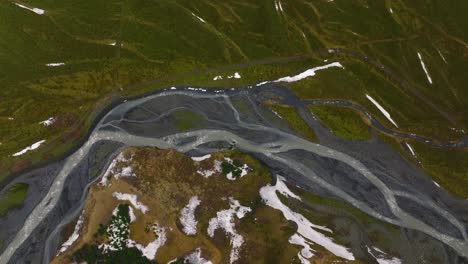 Luftaufnahme-Eines-Flusses,-Der-Durch-Mit-Schmelzendem-Schnee-Bedeckte-Berge-Fließt,-An-Einem-Bewölkten-Und-Nebligen-Tag-In-Island