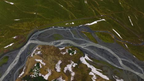 aerial top view of a river flowing through mountains covered in melting snow, on a cloudy and foggy day, in iceland