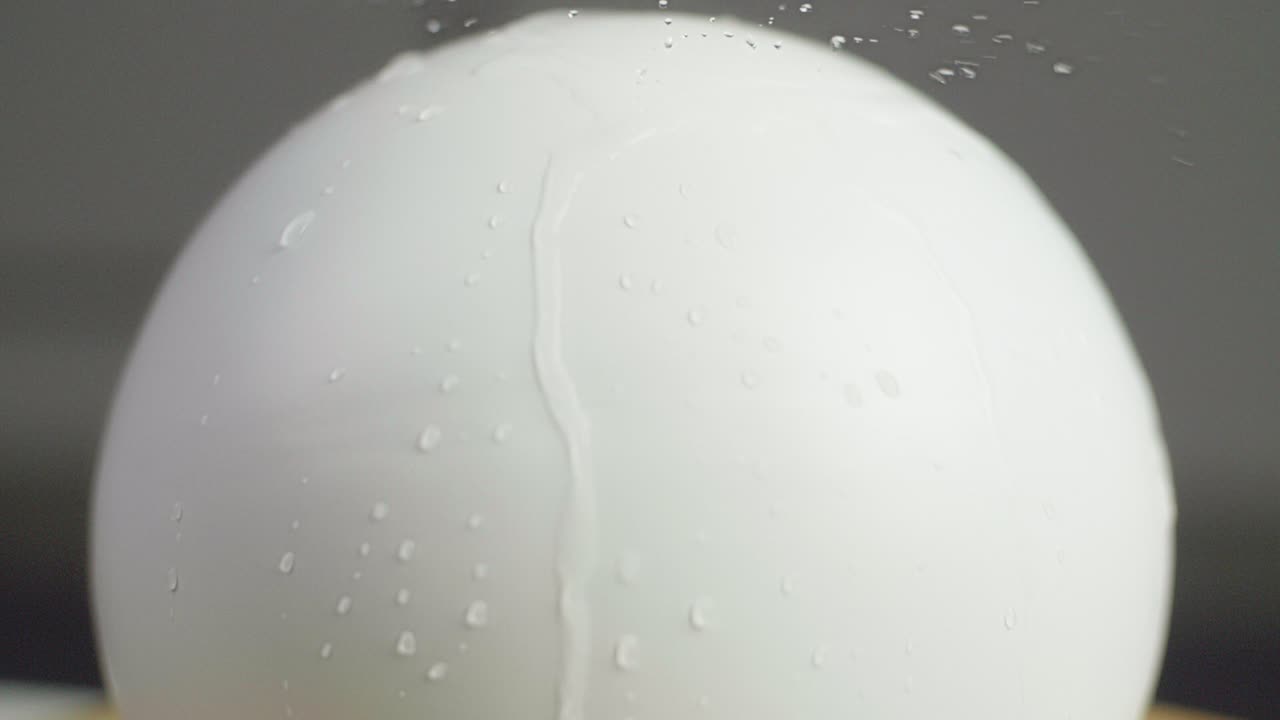 Close up of water falling on a plain white sphere with water srops on the sphere. A dark gray background. Shot in Slow Motion in 4K.