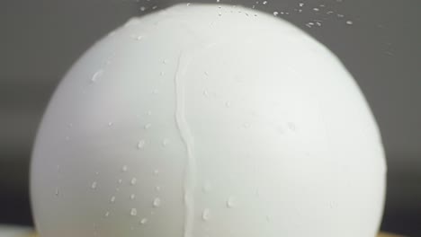 close up of water falling on a plain white sphere with water srops on the sphere. a dark gray background. shot in slow motion in 4k.