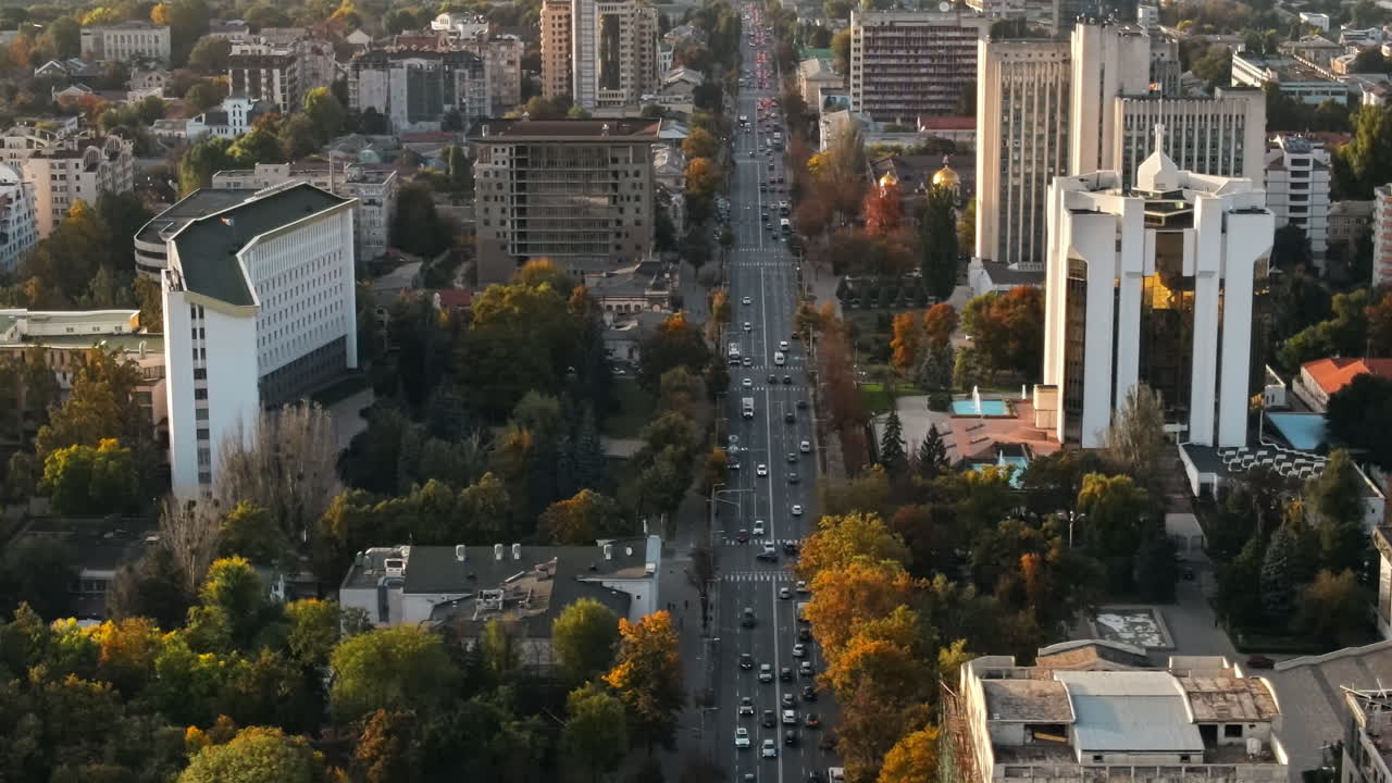 Aerial drone view of Chisinau downtown at sunset. Panorama view of multiple buildings, Parliament, Presidency, roads with moving cars and lush trees. Moldova