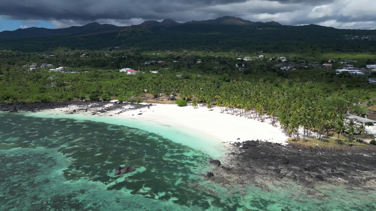 Aerial view of a tropical beach with palm trees, white sand, and volcanic rocks