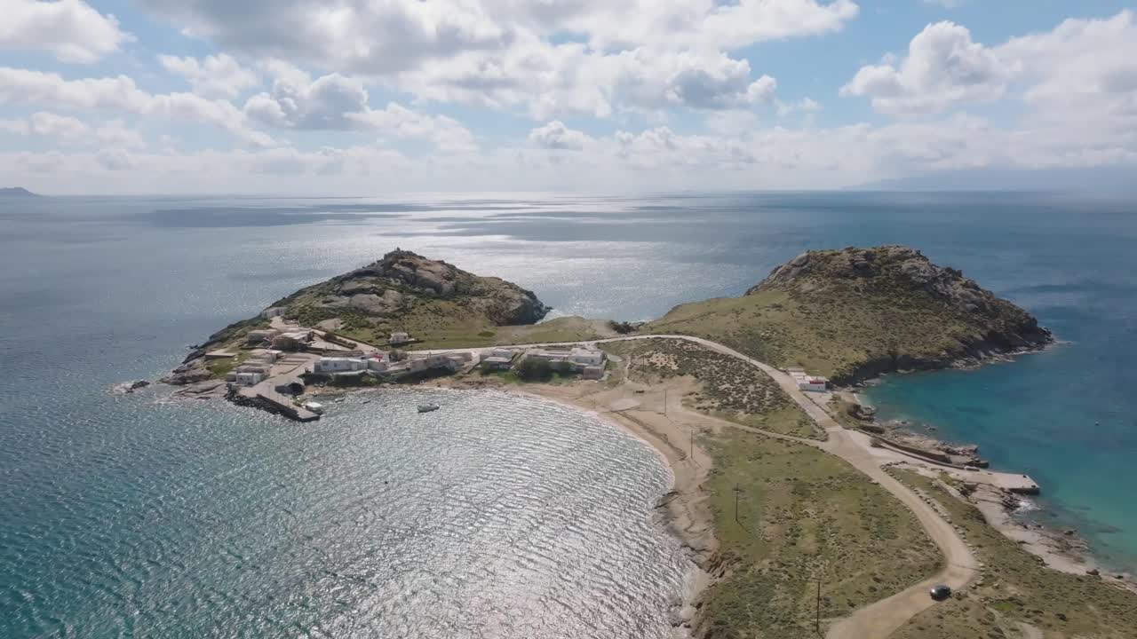 A cinematic orbiting drone shot of Divounia in Mykonos, showcasing its beach and the traditional fishing village by the Aegean Sea