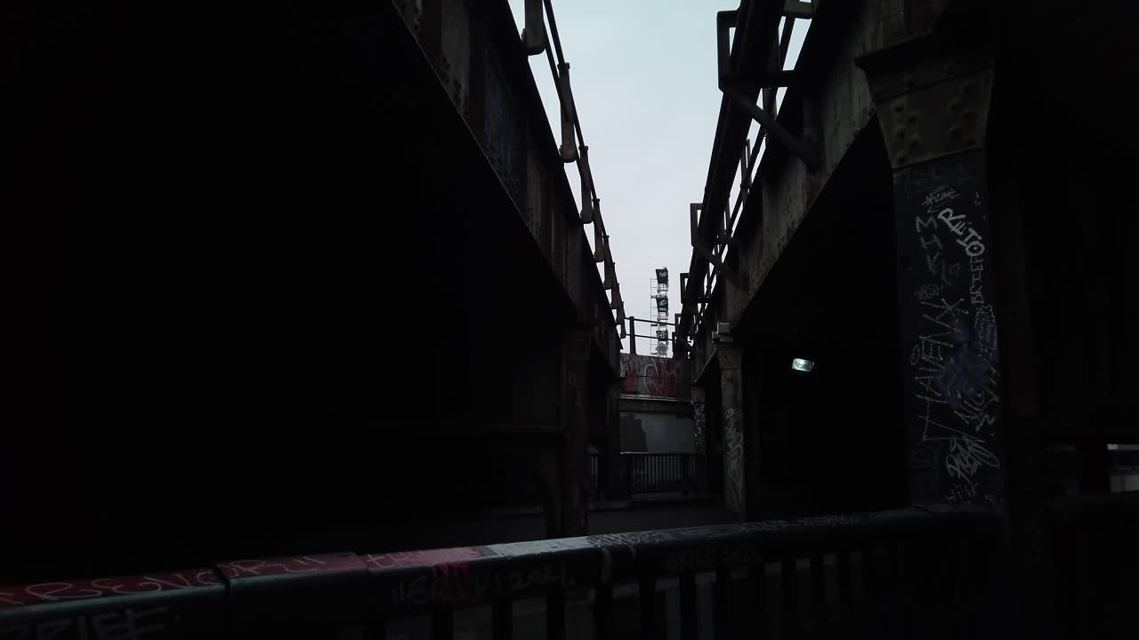 Old weathered railway bridge structure extending over an underpass, wide shot looking upwards with tilt down