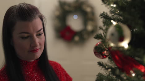 Smiling-woman-hangs-red-ornament-on-Christmas-Tree