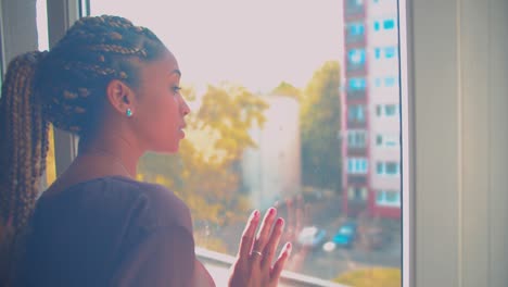 young sleepy mixed race woman looking outside through room window with sadness