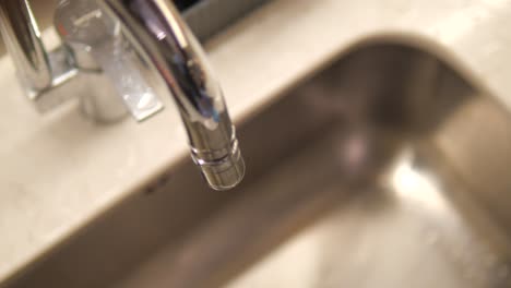 close up of a chrome faucet dripping water into a sink