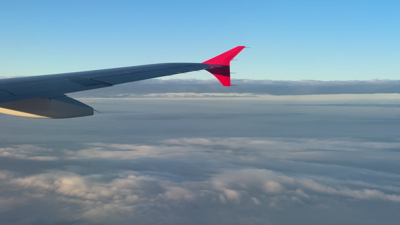 Vue depuis le hublot d'un avion montrant une aile au-dessus d'une couche de nuages avec l'horizon visible pendant le vol. Une lumière douce et un ciel calme créent une scène aérienne sereine.
