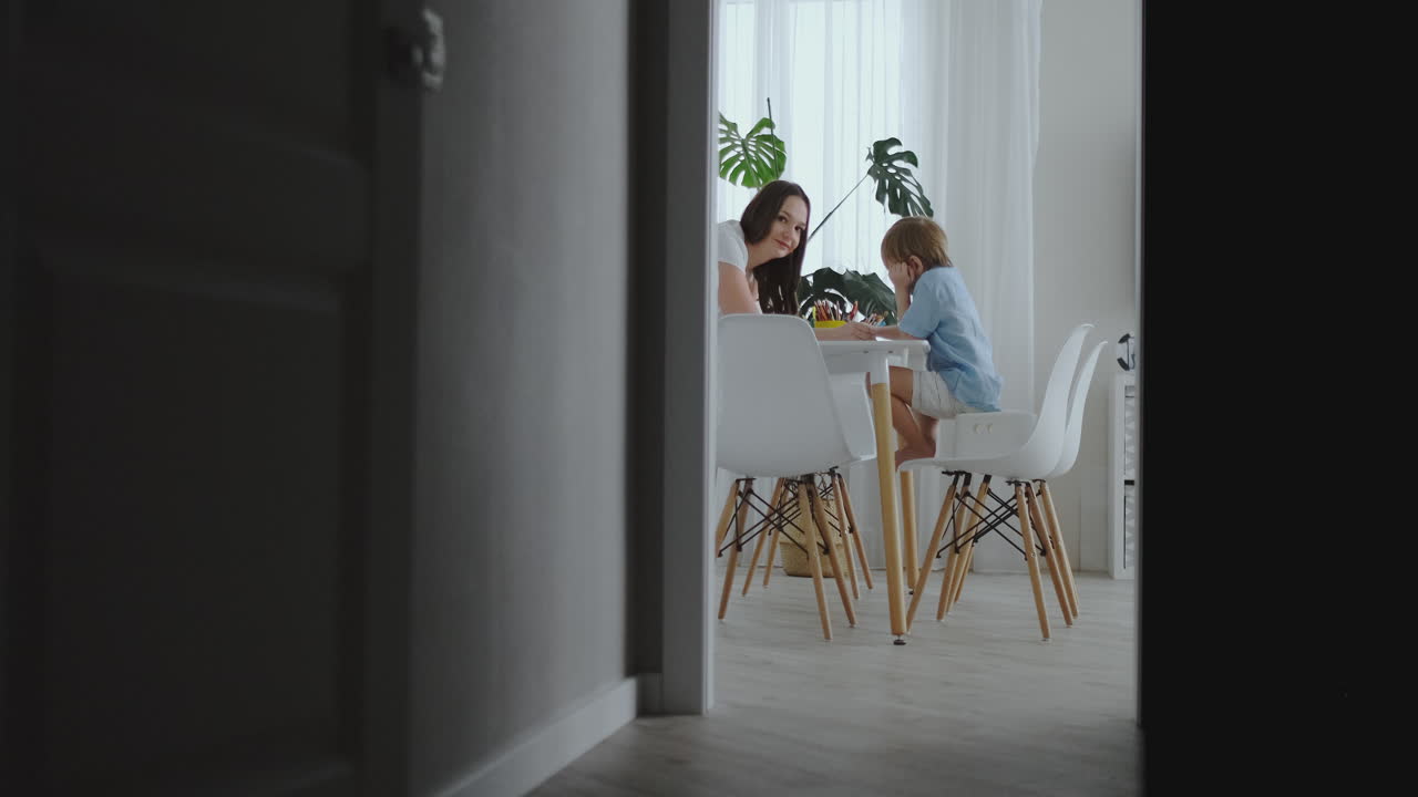 젊은 아름다운 어머니와 두 아들은 주방의 테이블에 앉아서 컬러 연필로 그림을 그리고 있습니다. 카메라는 느린 움직임으로 움직입니다.