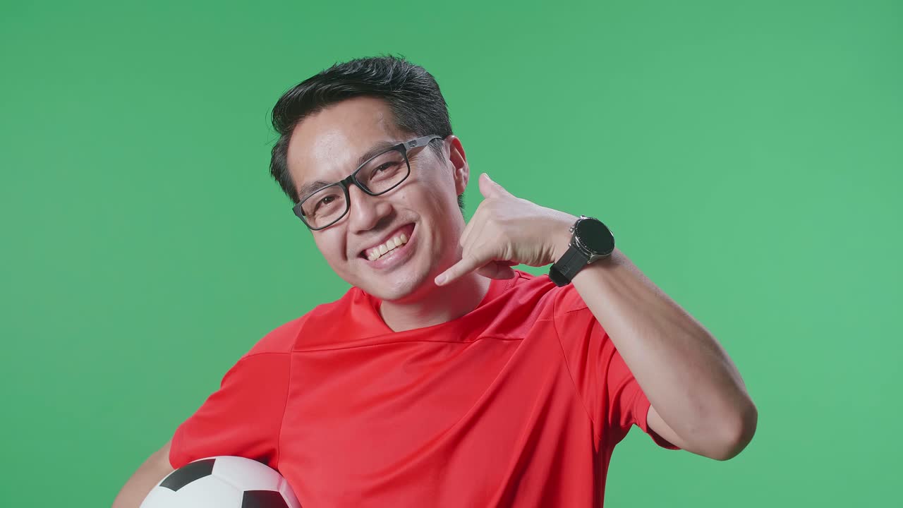 초록색 스크린 배경에서 축구를 응원하는 동안 공을 들고 미소 짓는 아시아 남자의 클로즈업