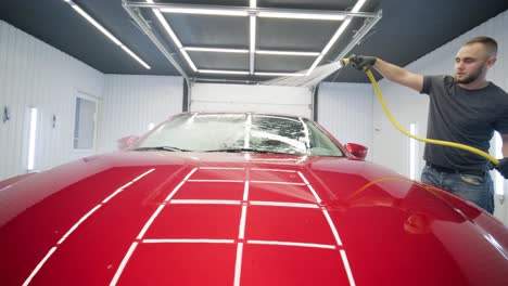 man worker washing red car on a car wash.