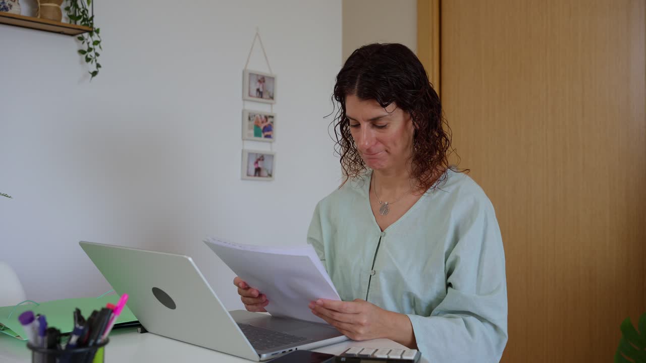 Mulher estressada sobrecarregada com papelada e problemas financeiros em casa.
