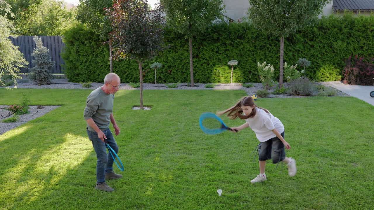 Active Grandfather Playing Outdoor Racket Game With Granddaughter In Backyard