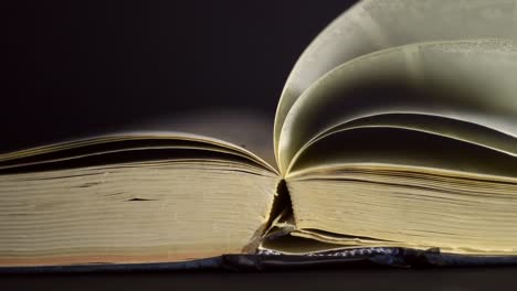 cámara lenta, primer plano de un libro antiguo, vintage, abierto con páginas girando en el viento, en una habitación oscura con poca luz, con un entorno negro