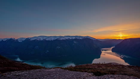 snow-capped mountains plunging into the water of the fjord far below during a colorful sunset - time lapse