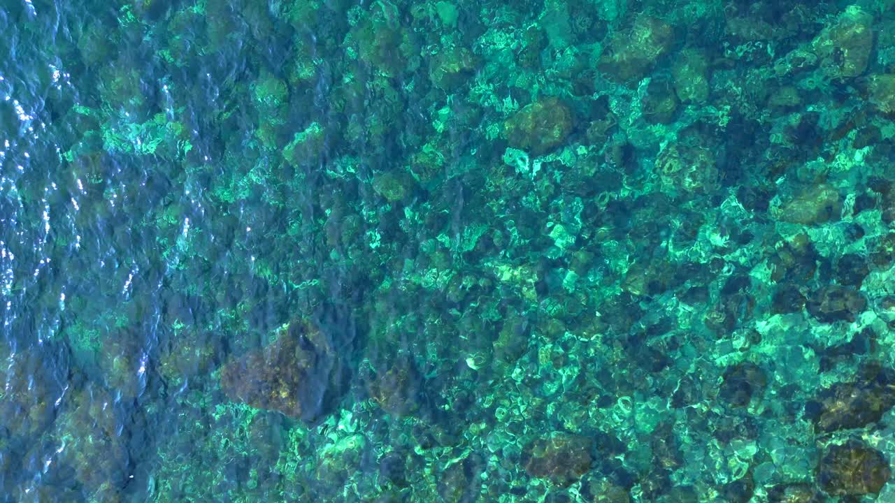 Transparent turquoise water flows between rocks in a bay in Ibiza, Spain. Spectacular aerial view flight vertical bird's eye view ascending drone