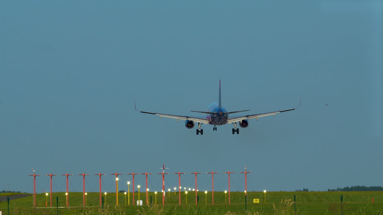 un avión comercial aterrizando en una pista con luces de navegación, campo verde en el fondo