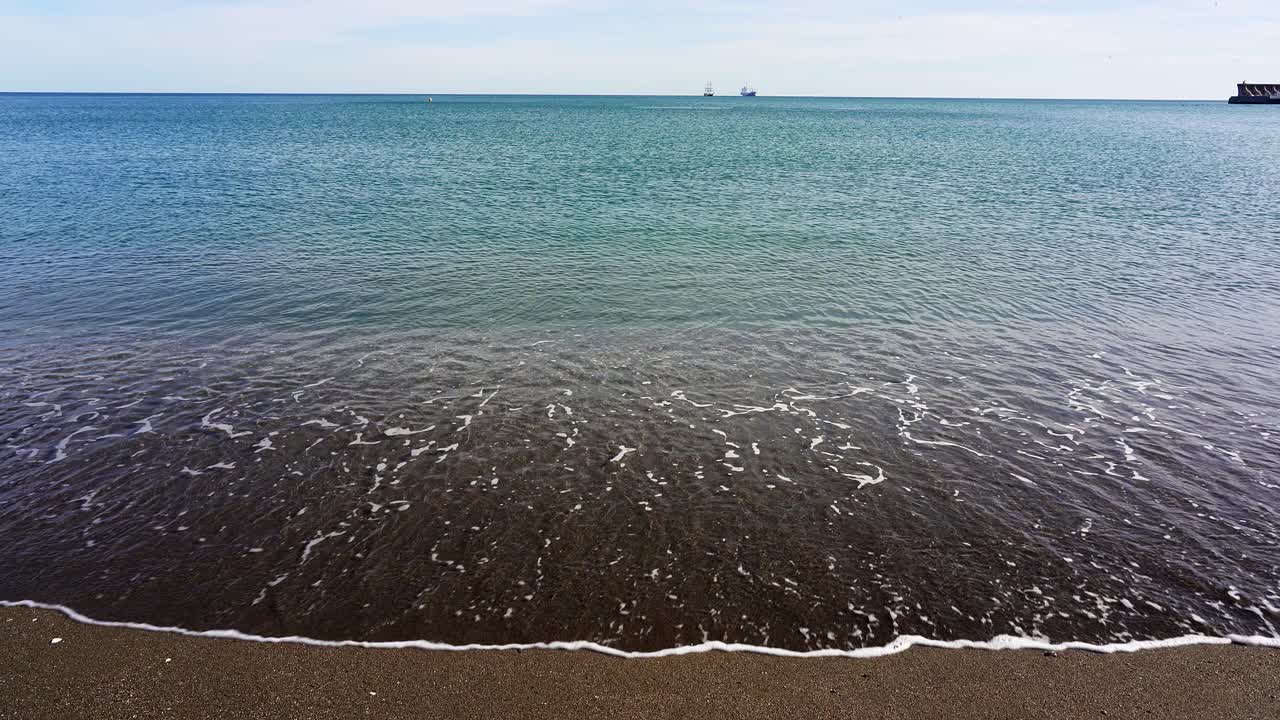 Onde accarezzano dolcemente la spiaggia sabbiosa della Malagueta a Malaga in una giornata di sole nella Costa del Sol in Spagna.