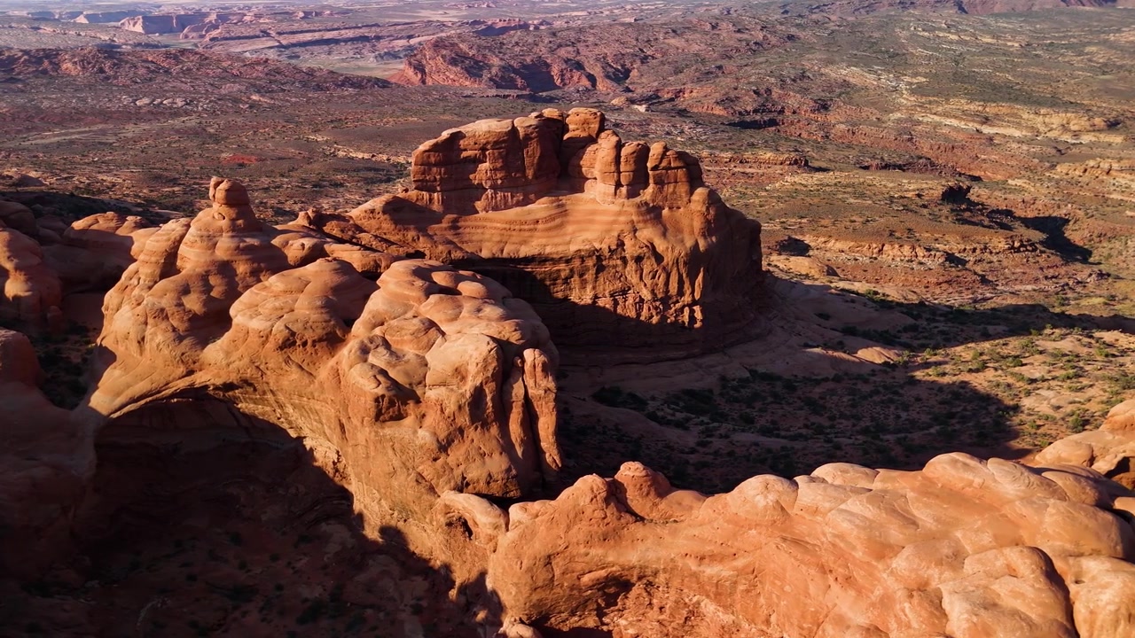 Splendido filmato stock del Parco Nazionale di Arches, USA, durante un pomeriggio luminoso. La luce solare brillante illumina le maestose strutture di arenaria rossa e il paesaggio desertico sotto un cielo azzurro limpido.