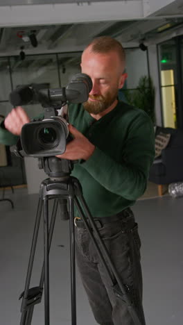 verticale video van een mannelijke filmcamera-operator die de camera van een statief haalt om een handheld film of video in een studio op te nemen