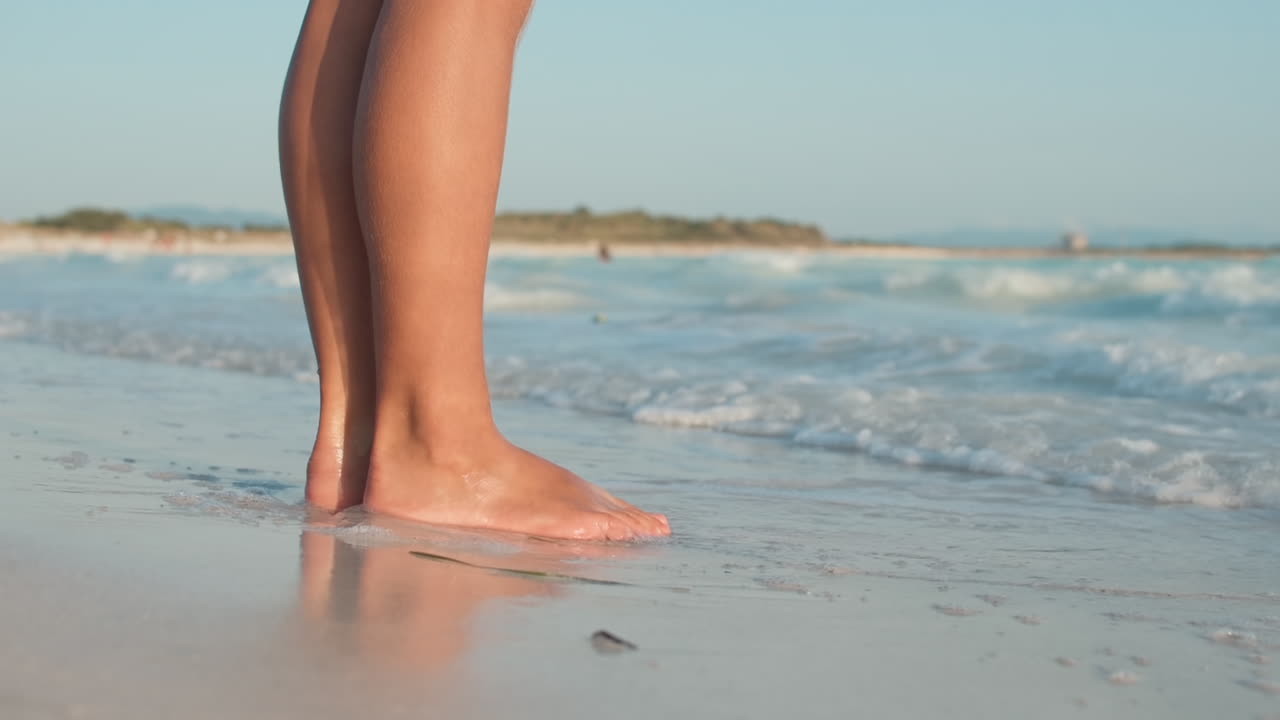 Onde del mare che si infrangono sulle gambe di una donna in spiaggia. Ragazza sconosciuta in piedi in riva al mare.