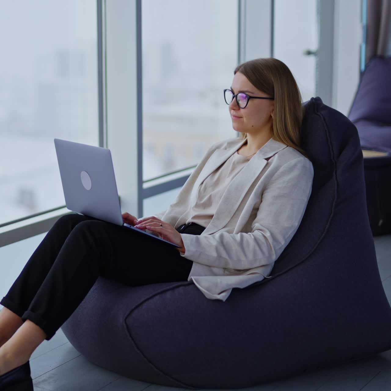 Freelance female entrepreneur working at laptop. Lady sits in comfortable chair near the big panoramic window