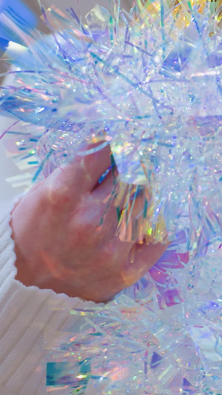 Close-up of female shopper holding shimmering tinsel and observing it thoughtfully in a decor store with bokeh lights in the background