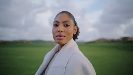 Portrait-serene-african-american-woman-looking-camera-at-green-meadow-view.