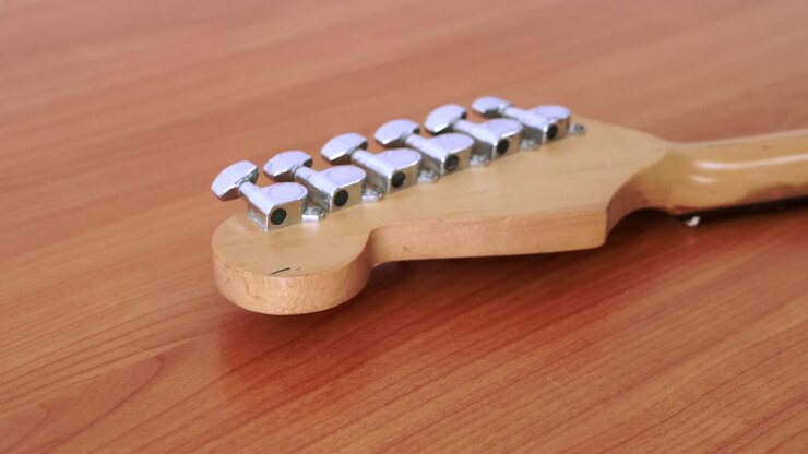 Ahşap bir masa üzerinde duran, ince gitar teli desenine sahip eski bir elektro gitarın kaydırma görüntüsü.