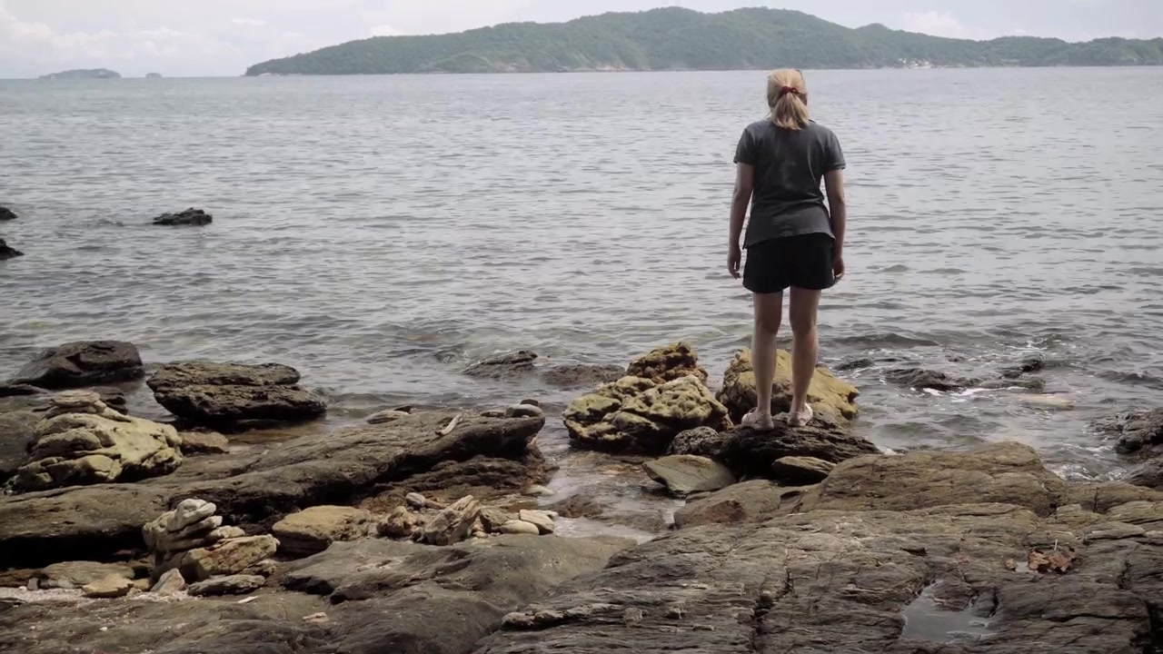 Una viaggiatrice asiatica cammina con attenzione sulle rocce costiere mentre esplora la costa panoramica e frastagliata del Parco Nazionale di Khao Laem Ya Mu Ko Samet in Thailandia